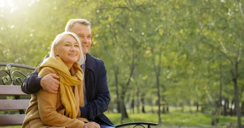 Datingsites: een man en een vrouw zitten dicht tegen elkaar op een bank in een groen park